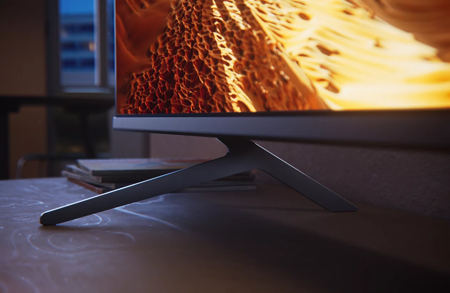 Primer plano de un televisor moderno con un soporte elegante sobre una mesa de madera, fondo borroso.