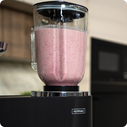 Czarny blender wypełniony różowym smoothie owocowym stoi na blacie.