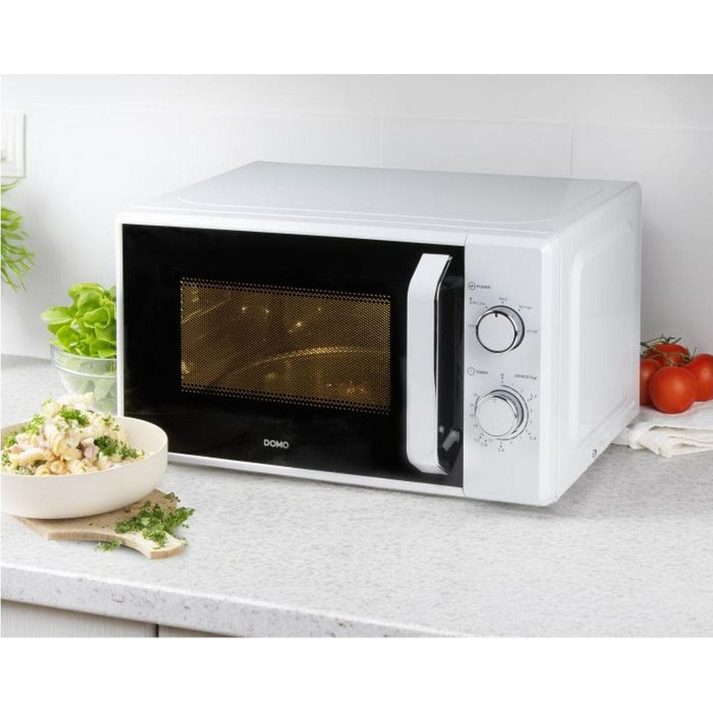 Un micro-ondes blanc est posé sur un plan de travail à côté d'un bol de salade et de tomates.