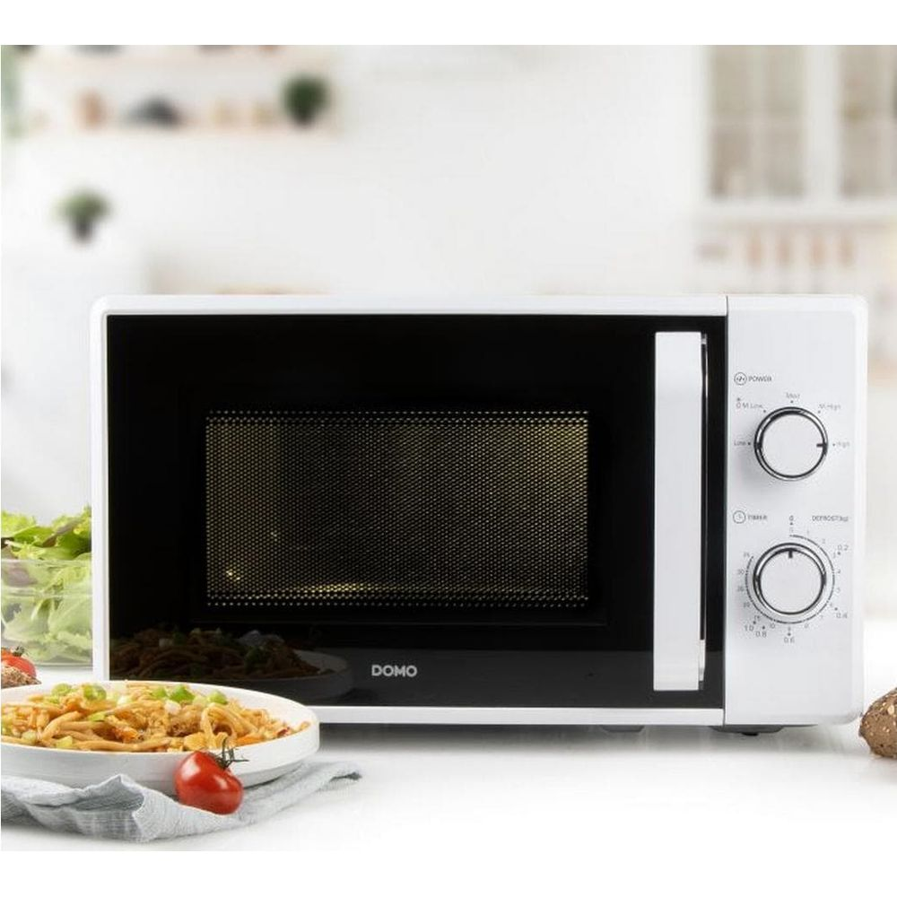 Un micro-ondes blanc avec deux boutons rotatifs sur un comptoir de cuisine devant un bol de nouilles.