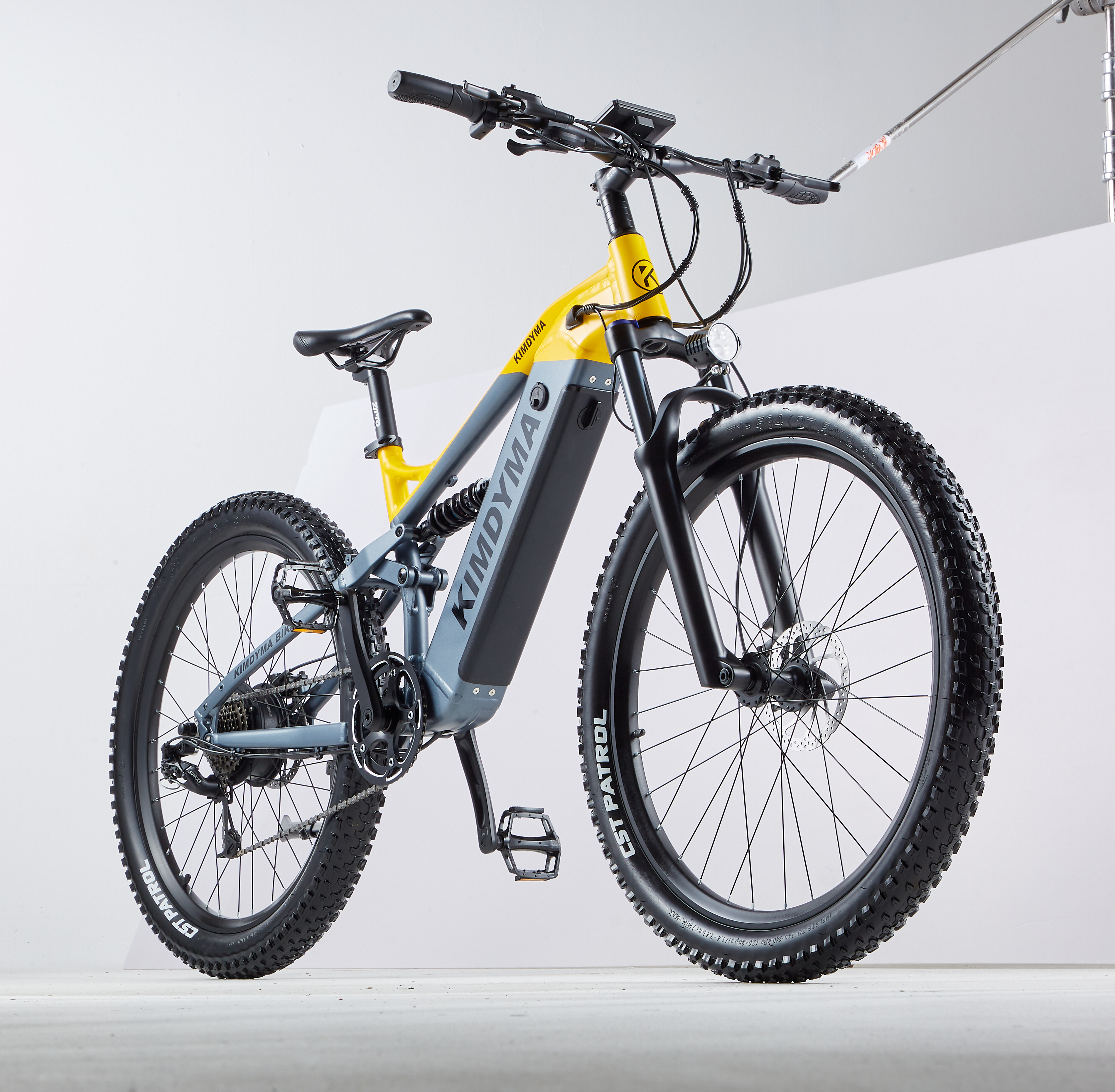 Una e-bike Kimdyma grigia e gialla con copertoni larghi in uno studio bianco.