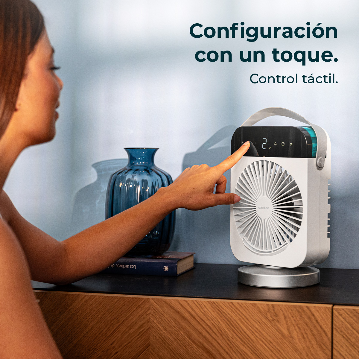 Una mujer toca el panel de control táctil de un ventilador de mesa blanco en un aparador de madera.