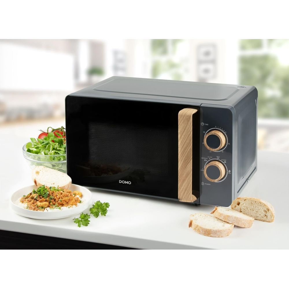 Micro-ondes gris avec accents en bois sur comptoir blanc, près de salade et pain.