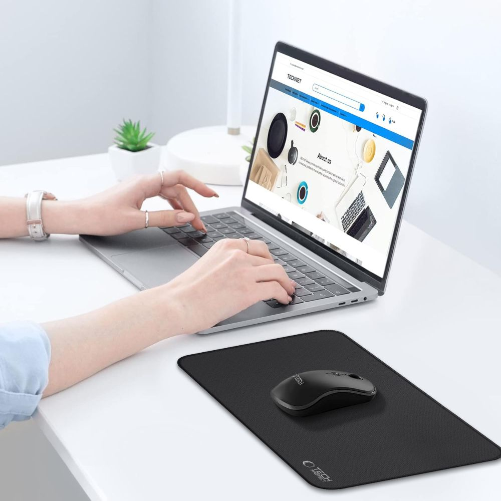 Iemand typt op een laptop terwijl een zwarte muis op een muismat op een wit bureau ligt.