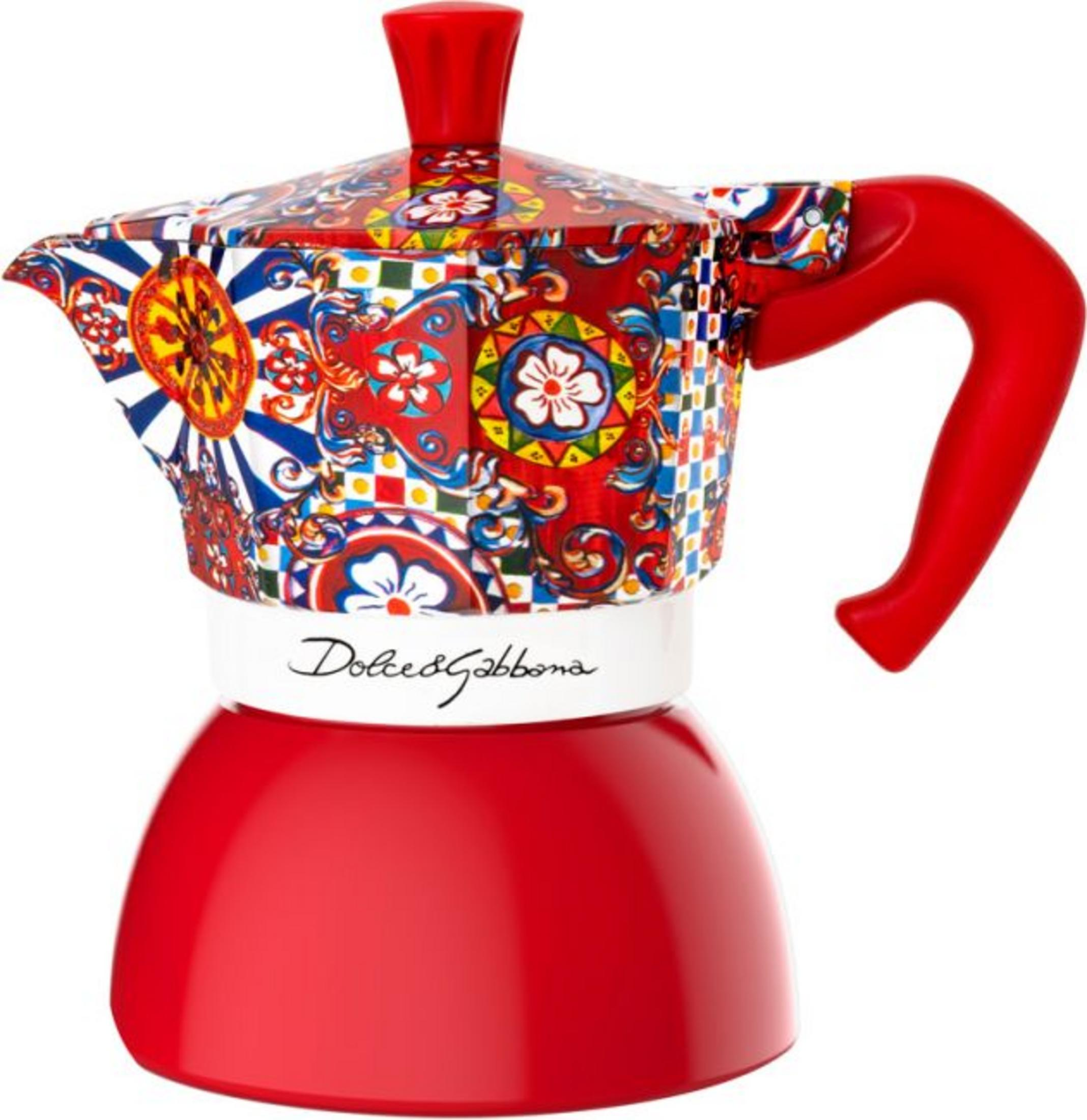 Una colorida cafetera moka con asa y base rojas, diseño de Dolce&Gabbana sobre una franja blanca.
