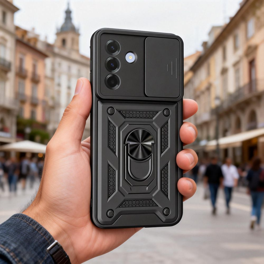 Eine Hand hält ein schwarzes Smartphone mit Schutzhülle und Ringhalterung vor einer verschwommenen Straßenkulisse.