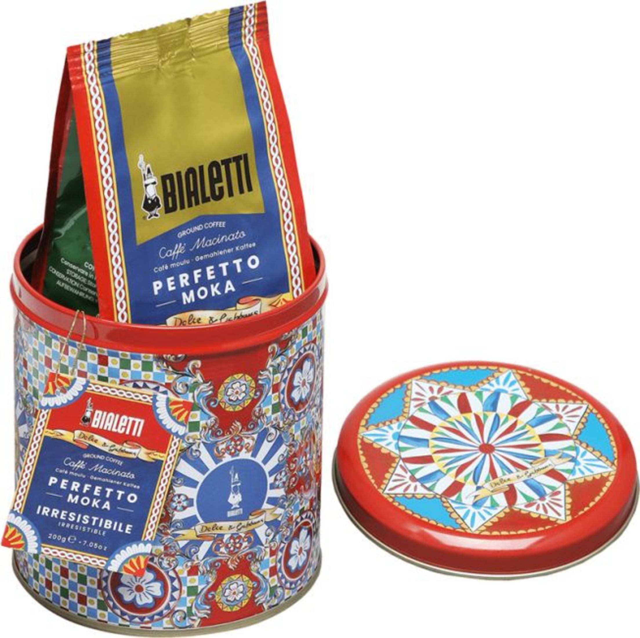 Latta di caffè Bialetti con motivi colorati e sacchetto di caffè, con coperchio accanto.