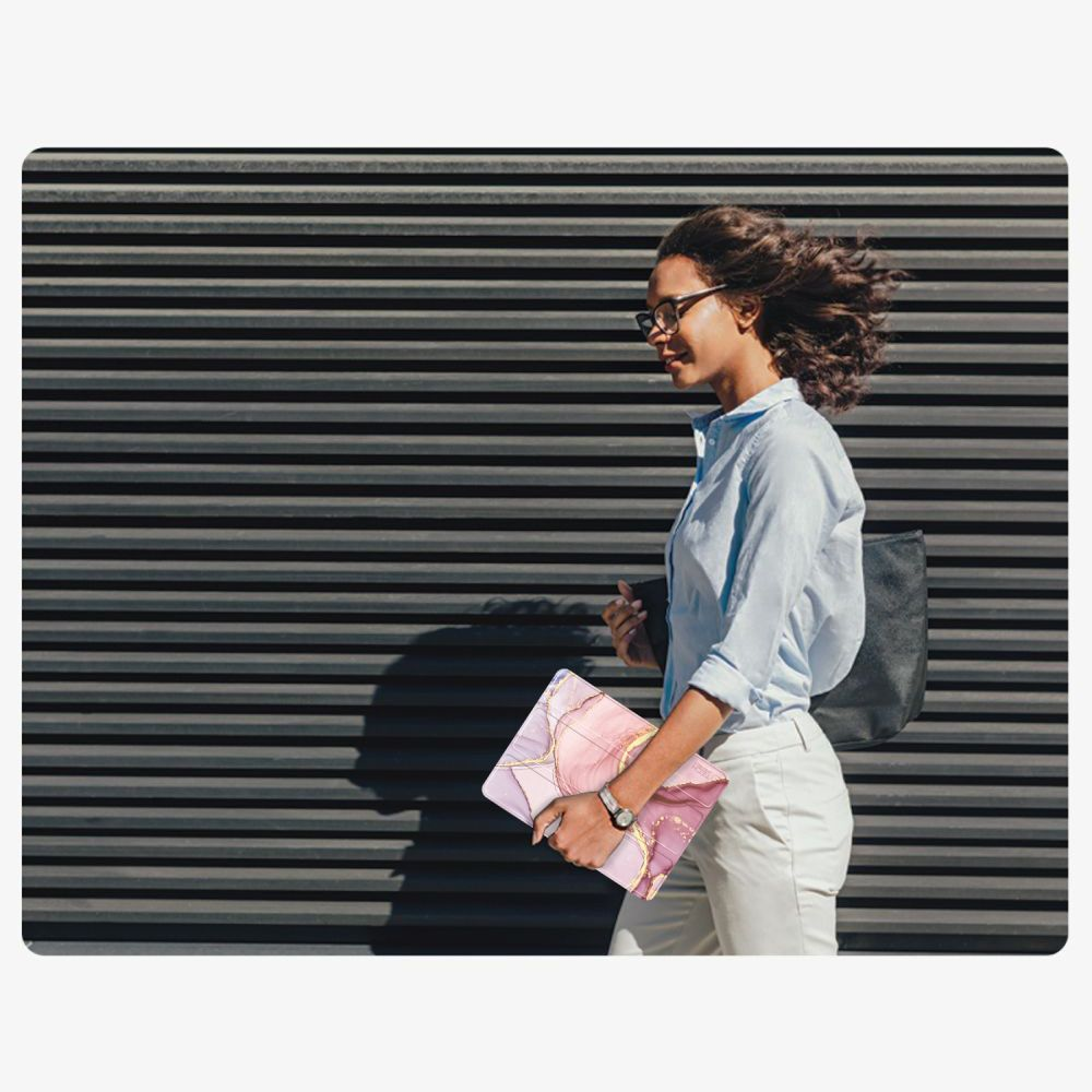 Una donna cammina davanti a una parete a doghe scure, tenendo una custodia per laptop rosa.