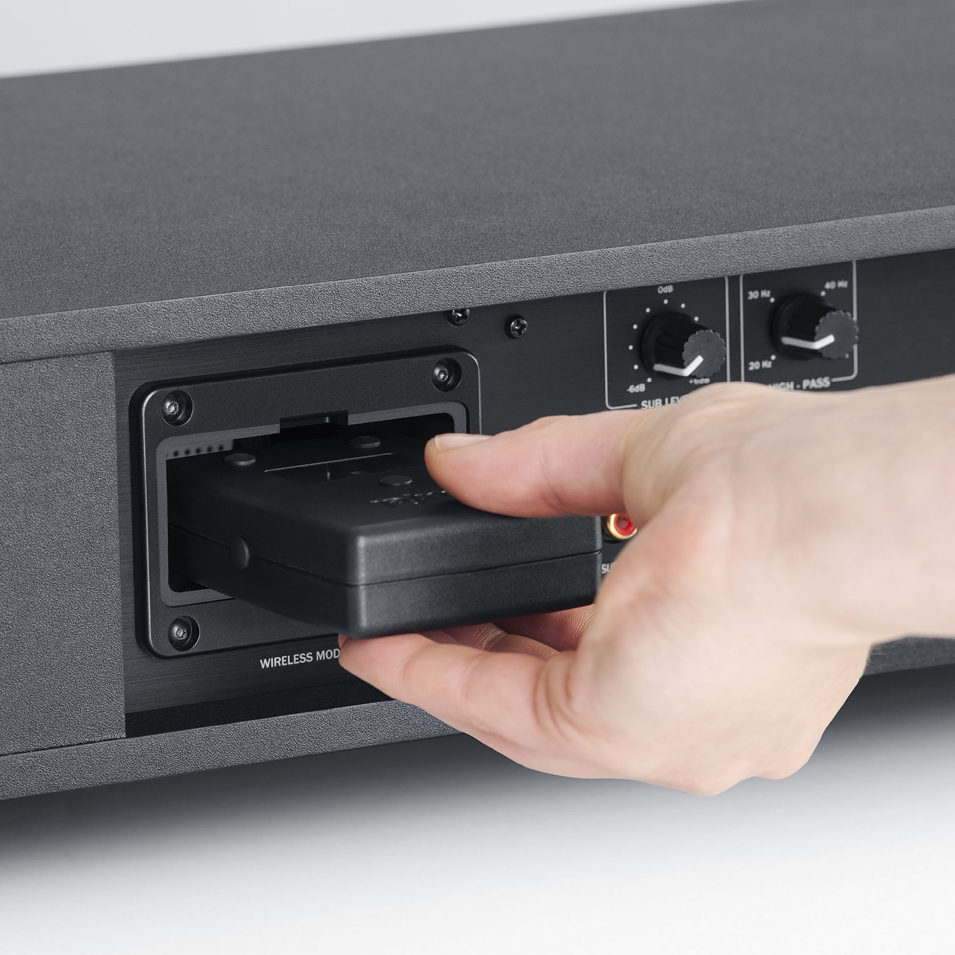 Une main insère un émetteur noir dans le logement du module sans fil d'un appareil audio.