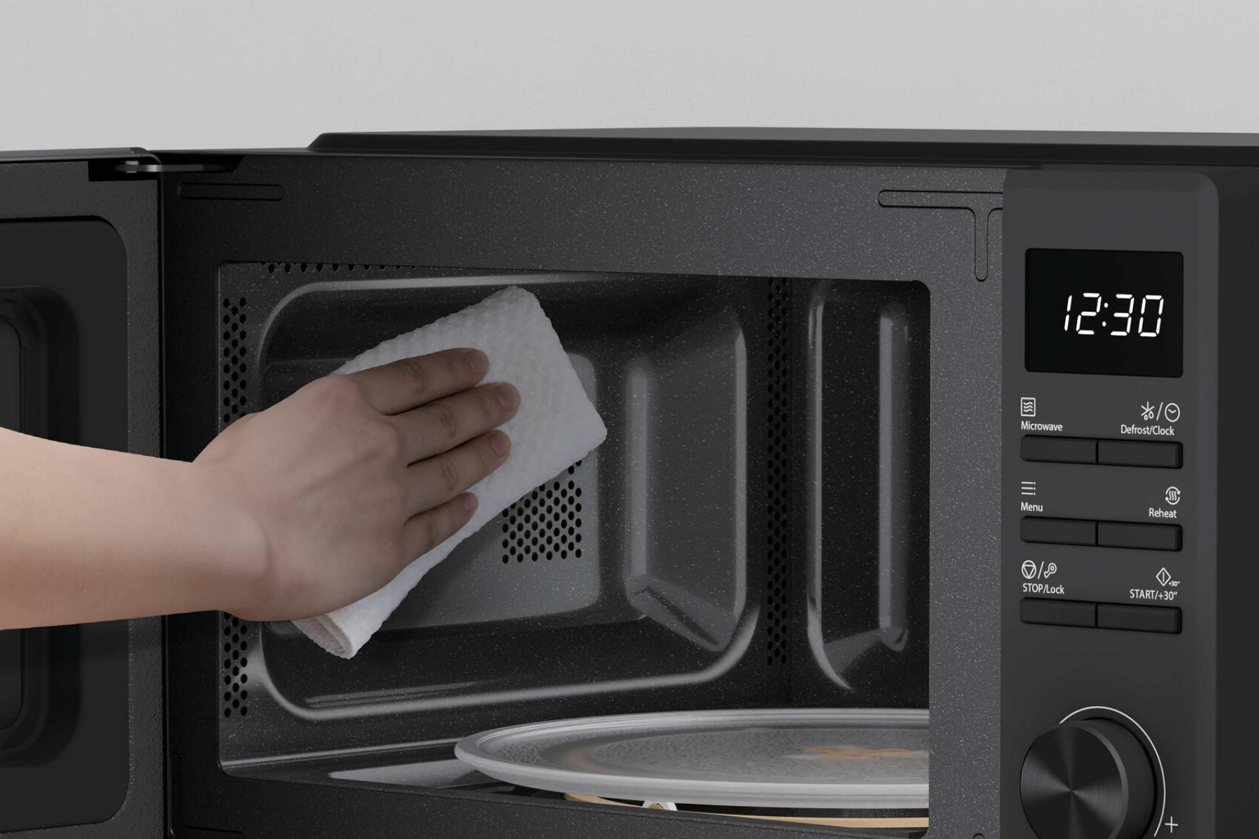 Una mano limpia el interior de un microondas negro con un pa#o blanco.
