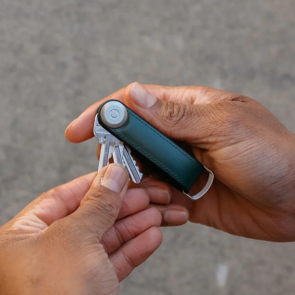 Para rąk otwiera ciemnozielony skórzany organizer do kluczy.