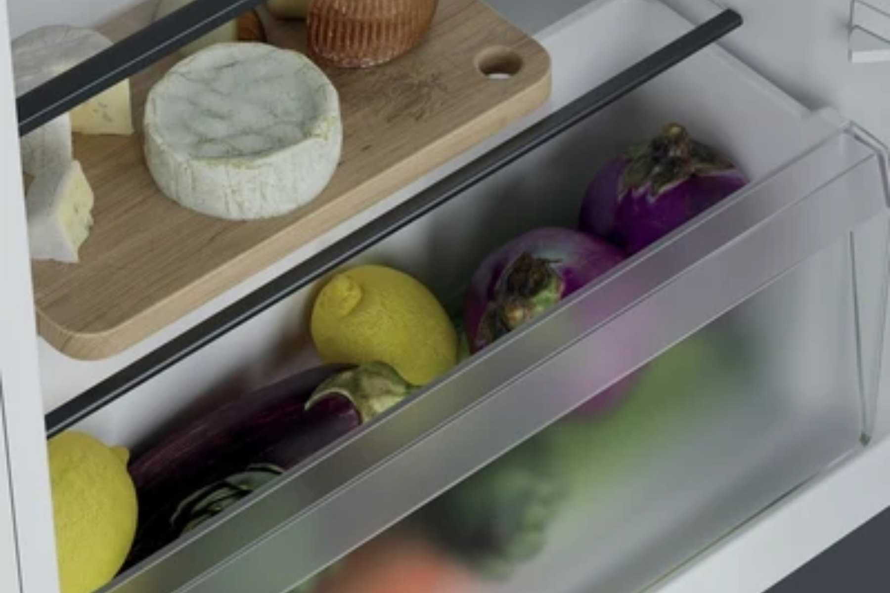 Cajón de refrigerador abierto con berenjenas y limones, y tabla de queso arriba.