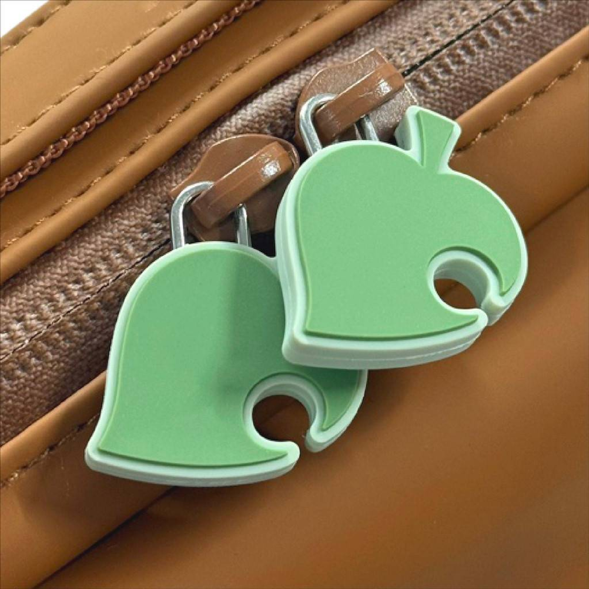 Dos tiradores de cremallera en forma de hoja verde en un bolso marrón.