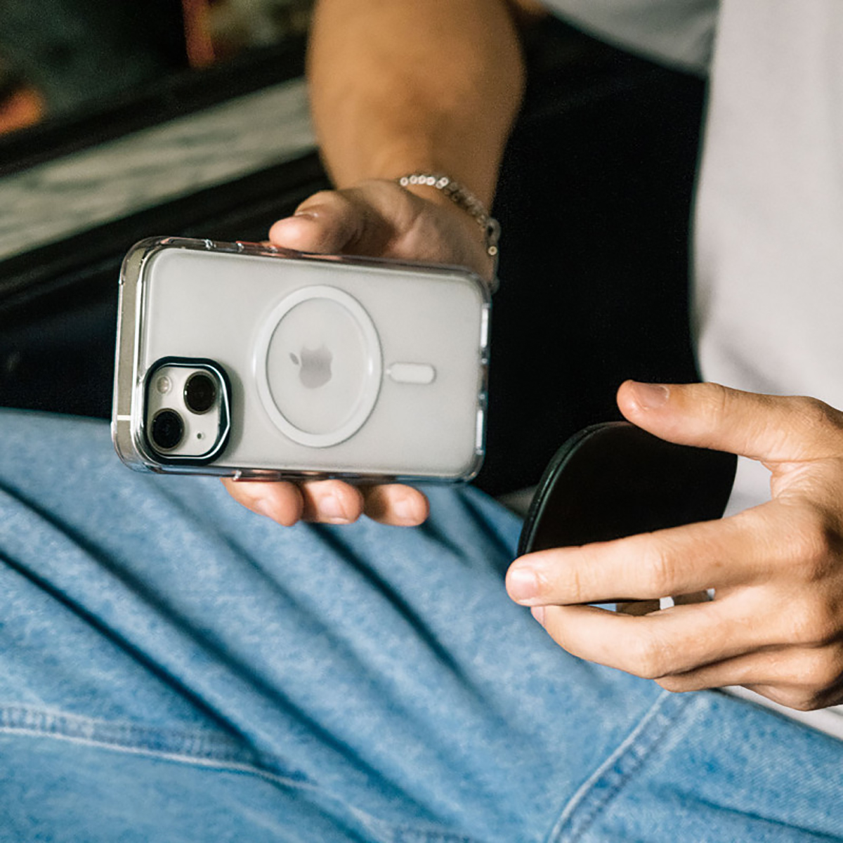 Eine Person hält ein Handy in transparenter MagSafe-Hülle und eine schwarze Magsafe-Brieftasche.