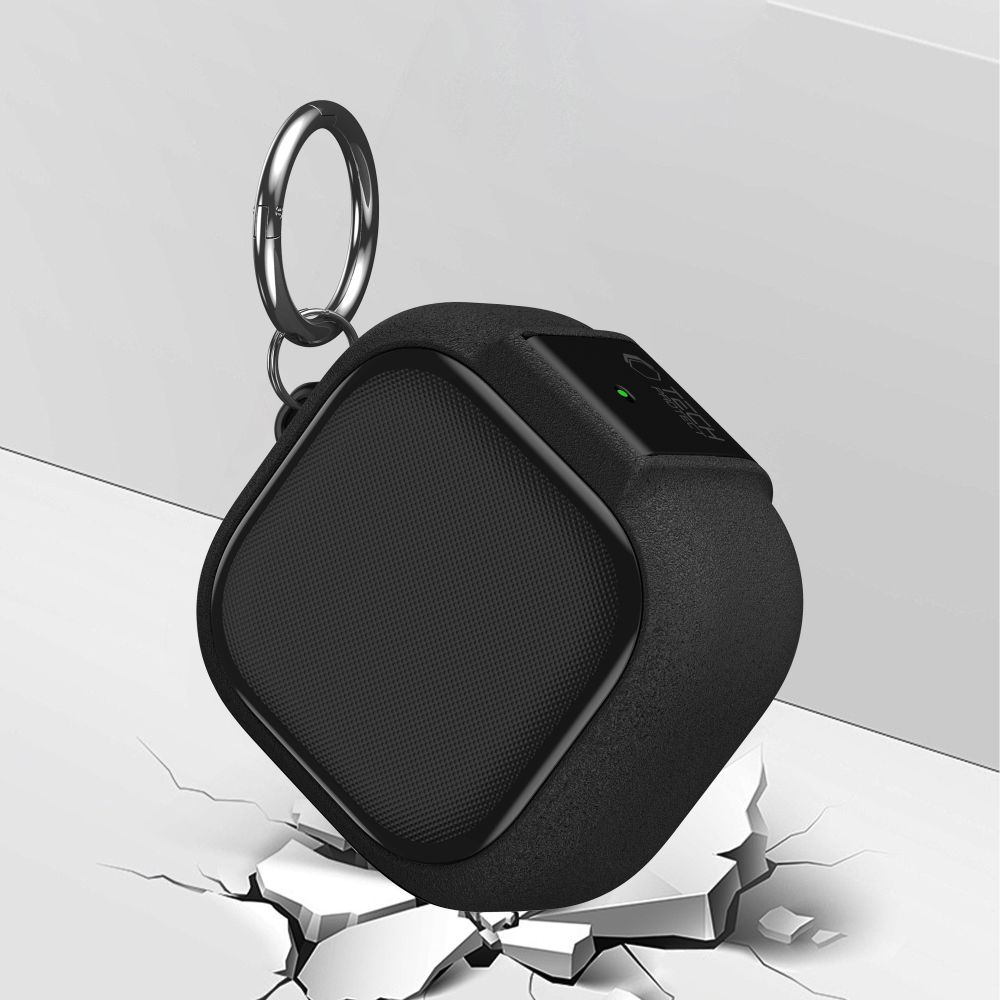 Ein schwarzer, quadratischer Bluetooth-Lautsprecher mit Karabinerhaken steht auf einer aufgebrochenen weißen Oberfläche.