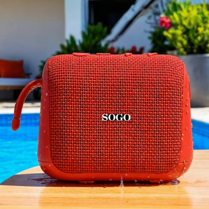Un altoparlante bluetooth SOGO rosso su un tavolo di legno vicino a una piscina, con piante sullo sfondo.