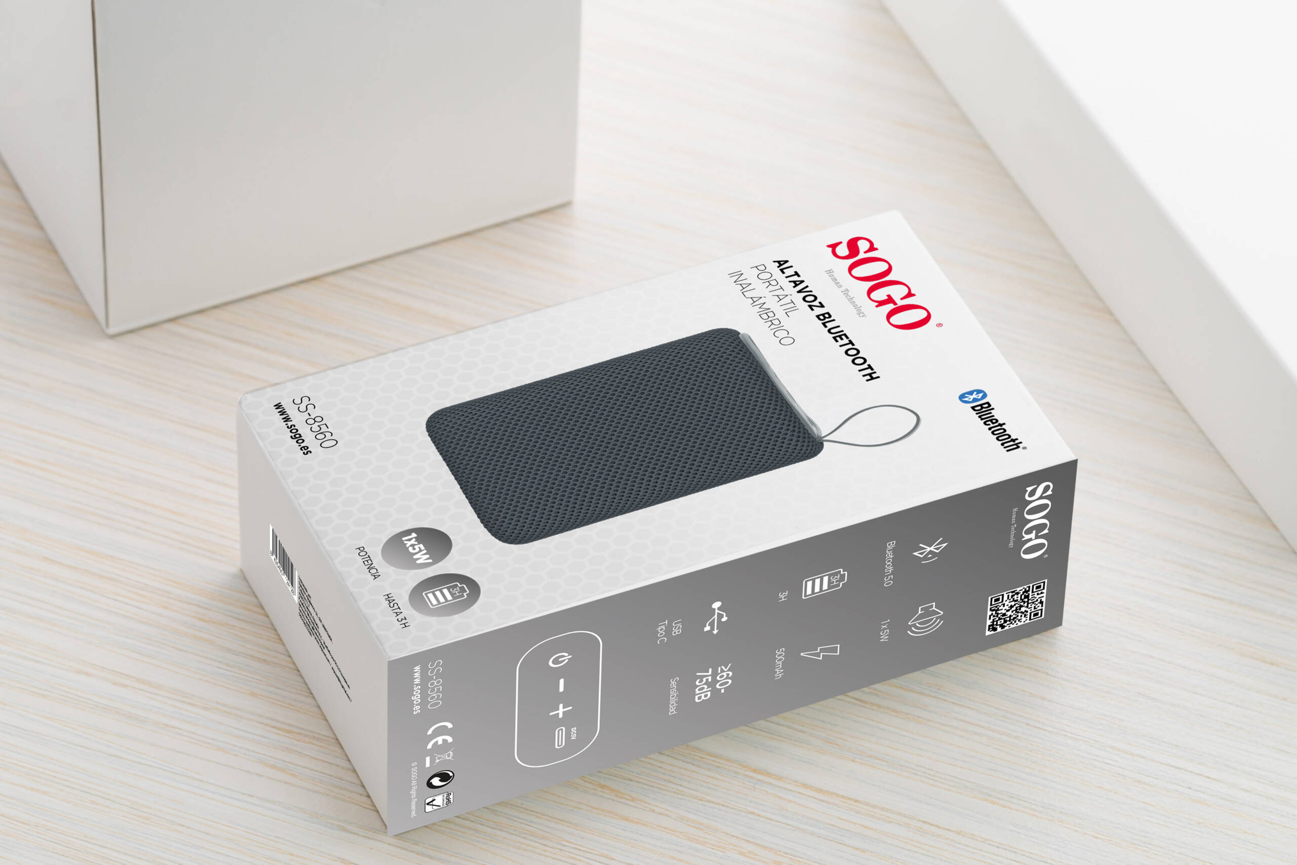 Una scatola bianca e grigia per altoparlante Bluetooth portatile SOGO su un tavolo in legno chiaro.