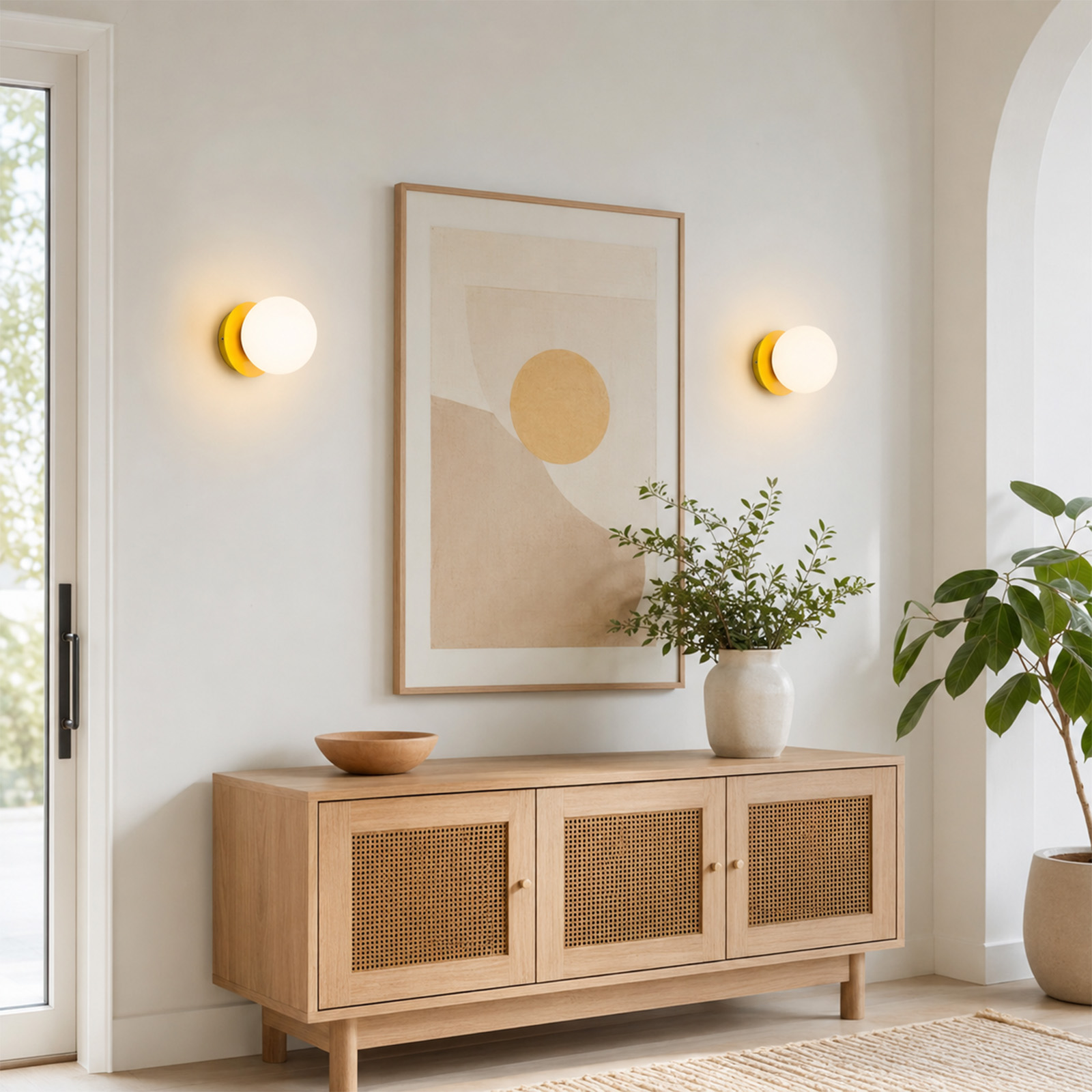 Un aparador de madera con puertas de ratán bajo un cuadro abstracto, flanqueado por dos apliques redondos.