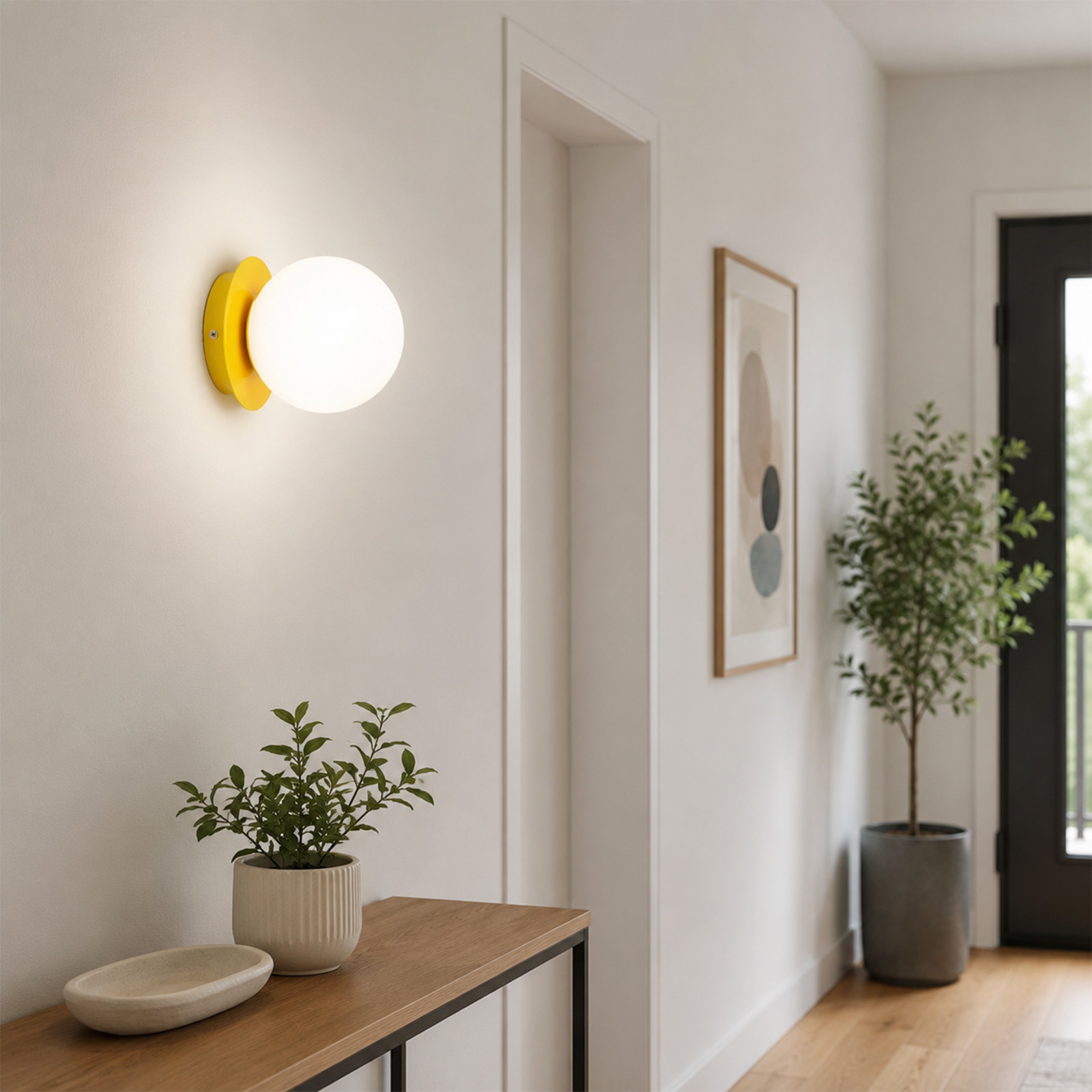 Una pared de pasillo luminosa con un aplique redondo amarillo, consola de madera con planta, cuadro y puerta.