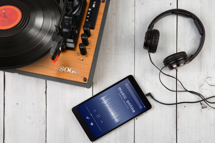 Un giradischi, delle cuffie e un tablet con un'app musicale su un tavolo di legno.