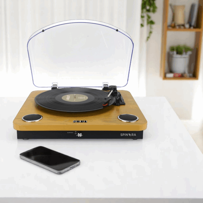 Un giradischi in legno con un disco in vinile si trova su un tavolo bianco vicino a uno smartphone.