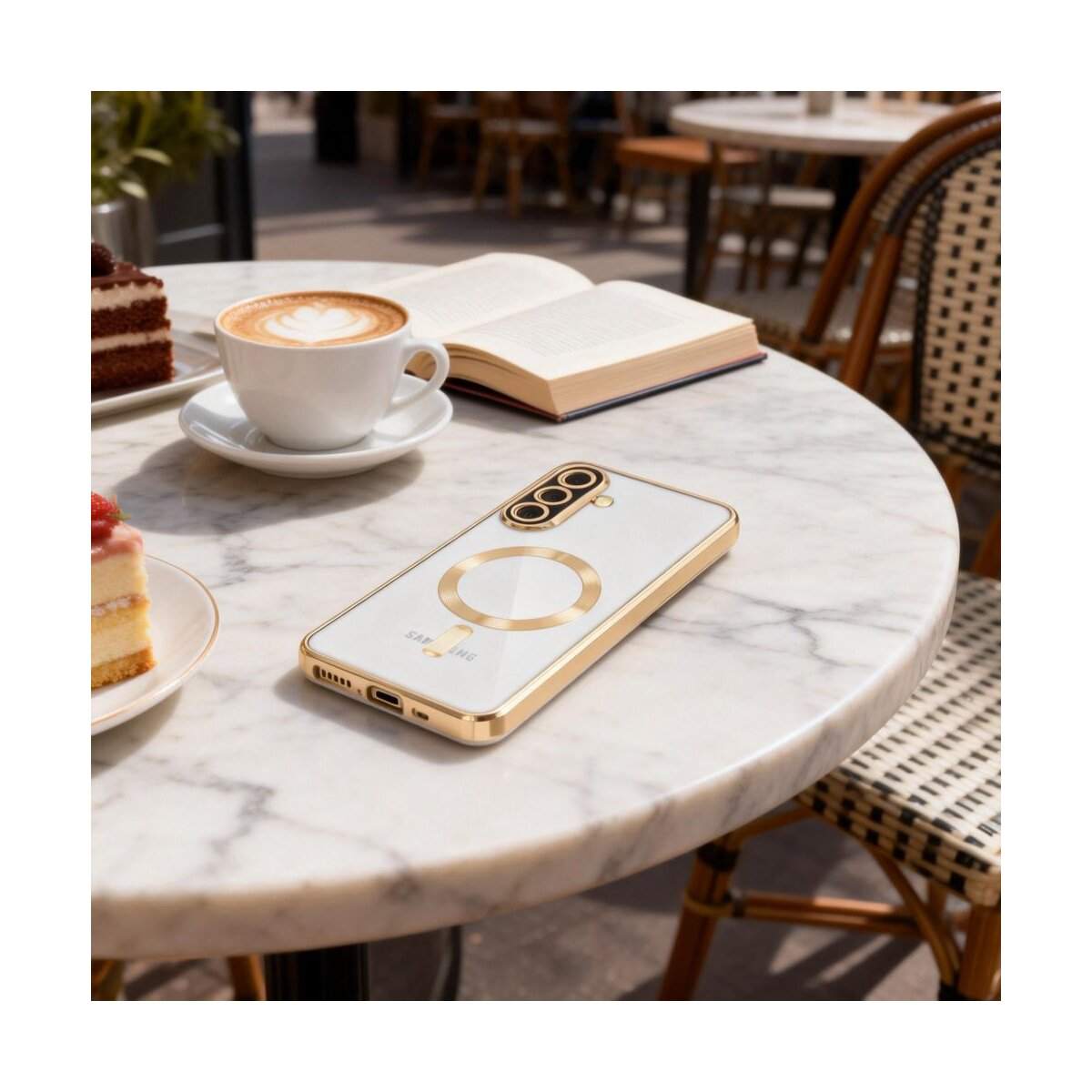 Ein Smartphone in einer goldenen Hülle, eine Kaffeetasse, Kuchen und ein Buch auf einem Marmortisch in einem Café.