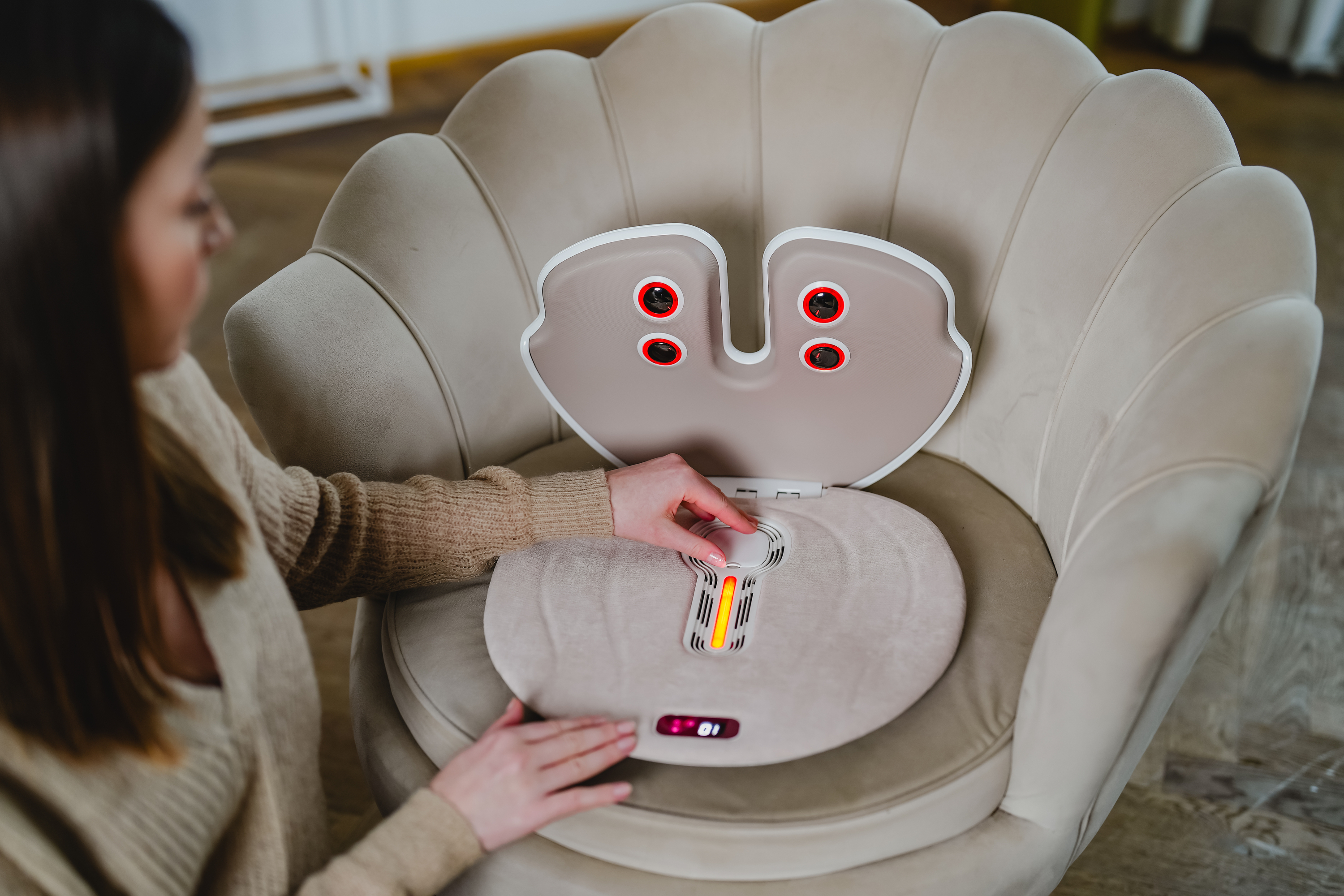 Una mujer opera un masajeador de pies beige en forma de mariposa en un sillón.