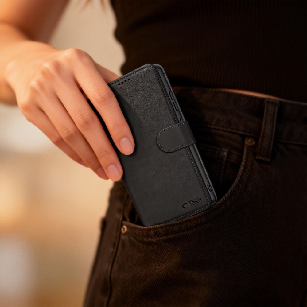 Eine Person steckt eine schwarze Leder-Handytasche in die Tasche ihrer dunklen Jeans.