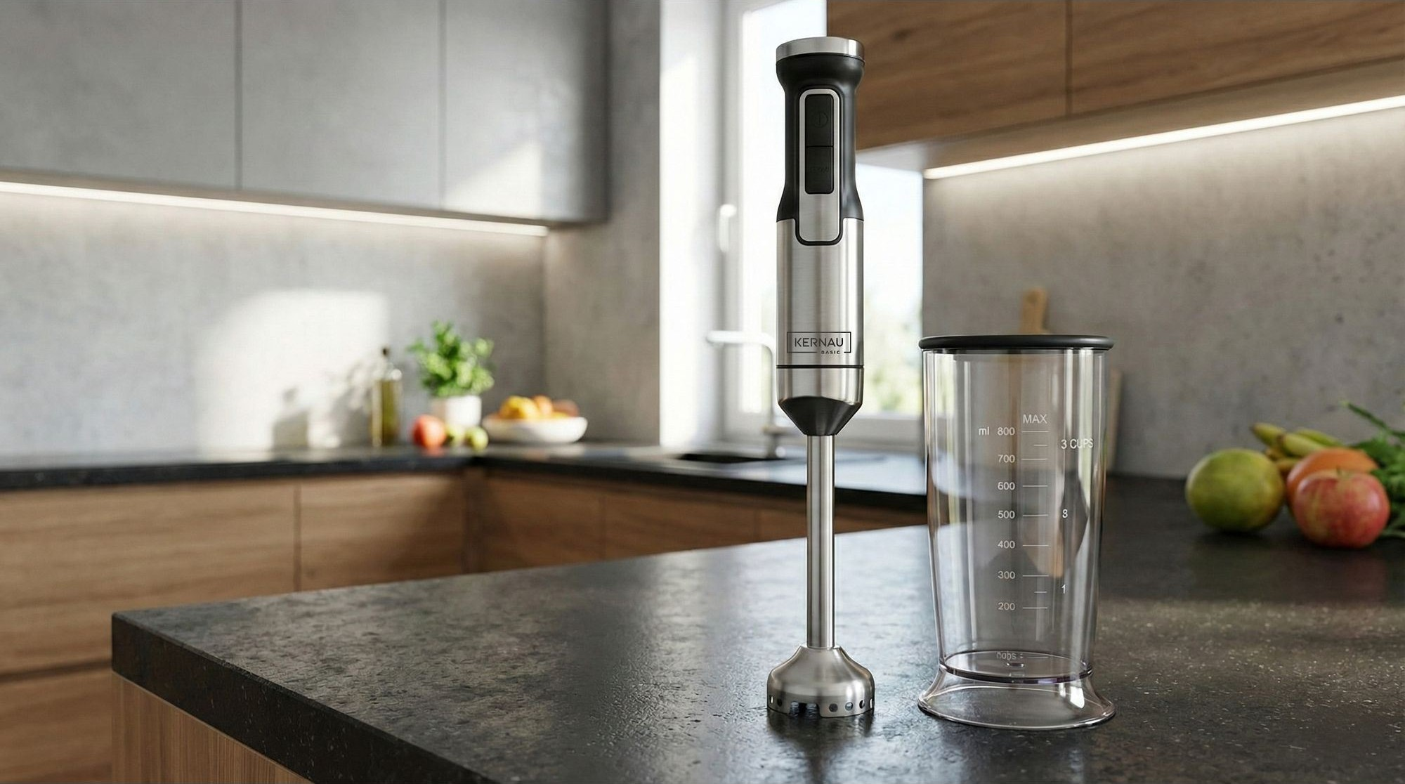 Srebrny blender ręczny i miarka stoją na ciemnym blacie w nowoczesnej kuchni.