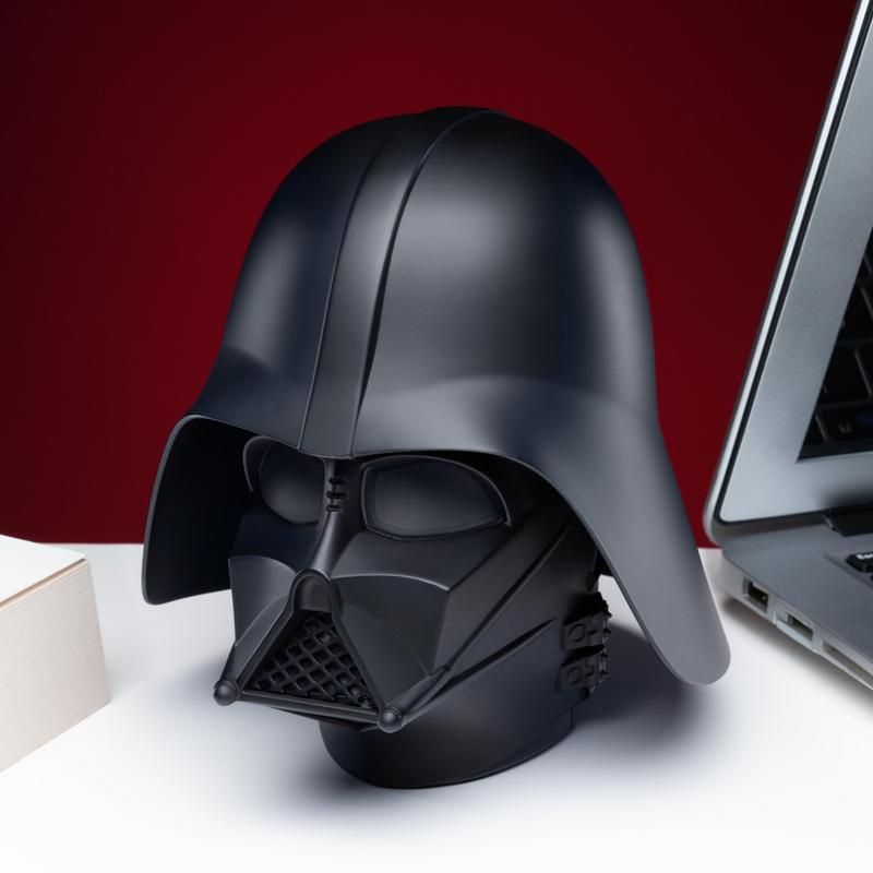 Un casco negro mate de Darth Vader en un escritorio blanco con fondo rojo.