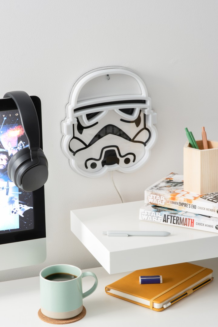 Una luz de pared iluminada de Star Wars Stormtrooper cuelga sobre un escritorio con un monitor y libros.