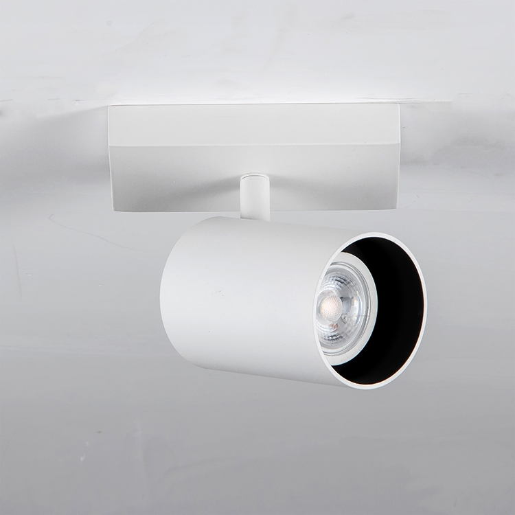 Un foco de techo blanco con un soporte cilíndrico y anillo interior negro en un techo blanco.