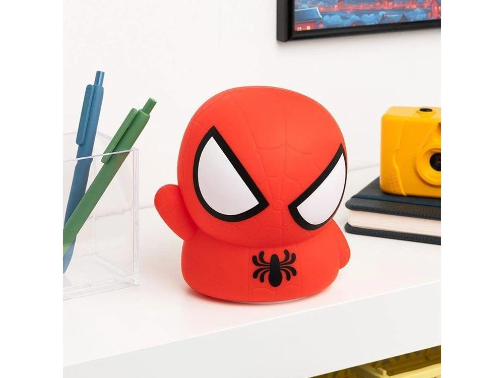Una luz nocturna roja de Spider-Man se encuentra en un estante blanco con bolígrafos, cuadernos y una cámara amarilla.