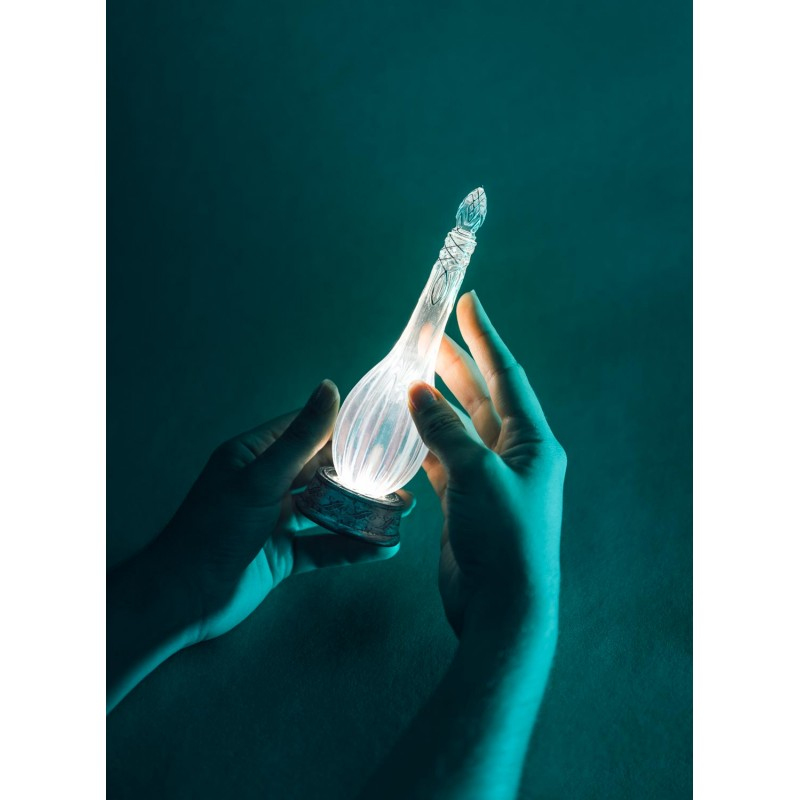 Manos sosteniendo un frasco de vidrio brillante sobre fondo oscuro.