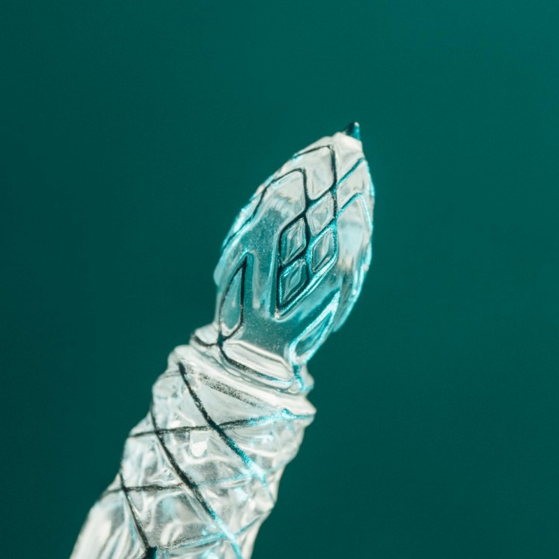 Un objeto de vidrio transparente tallado con patrones de diamantes sobre un fondo turquesa oscuro.