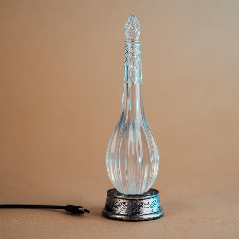 Una redoma de vidrio transparente con patrones plateados sobre una base de metal adornada y un cable USB conectado.