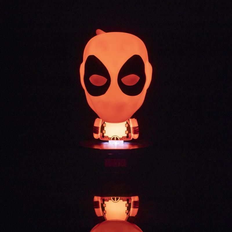 Una figura de Deadpool roja y brillante en la oscuridad con una fuente de luz cálida desde abajo y un reflejo.