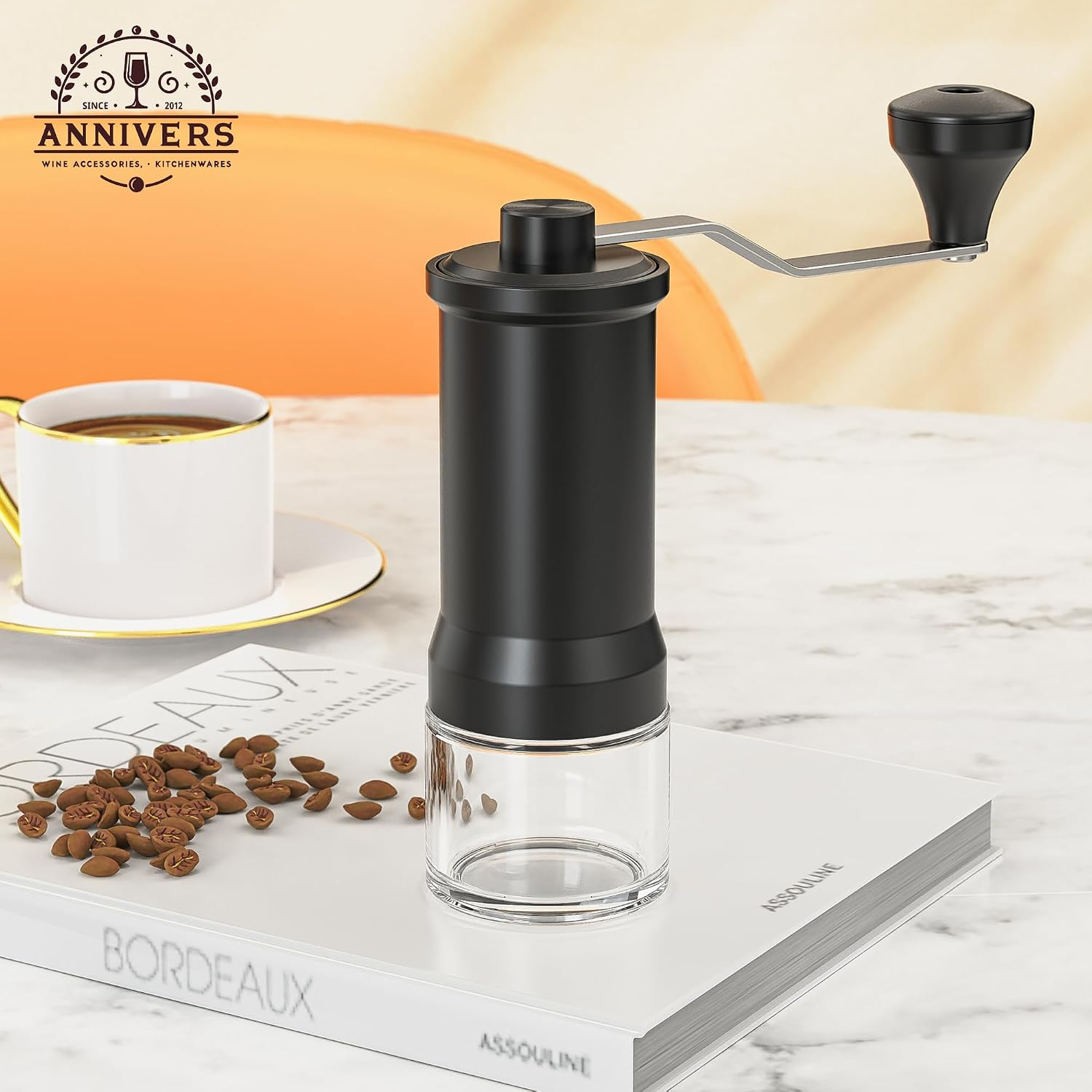 Eine schwarze Handkaffeemühle steht auf einem Buch, daneben Kaffeebohnen und eine Tasse Kaffee auf einem Marmortisch.