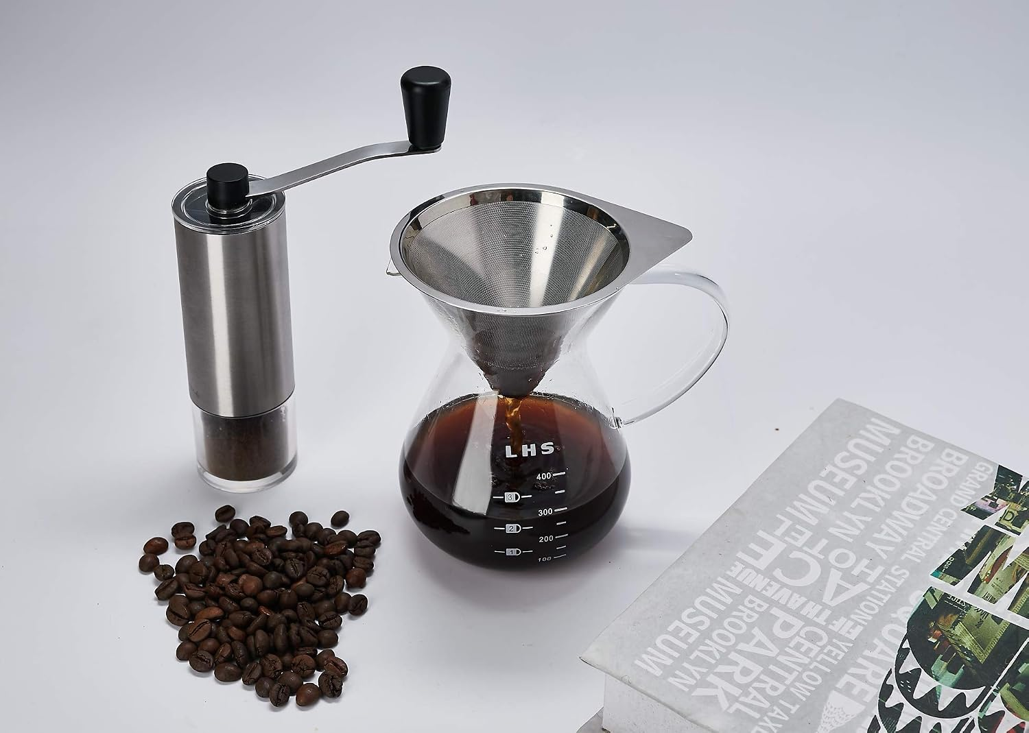 Handkaffeemühle, Kaffeebereiter mit Filter voll Kaffee, Bohnen und Buch auf weißem Tisch.