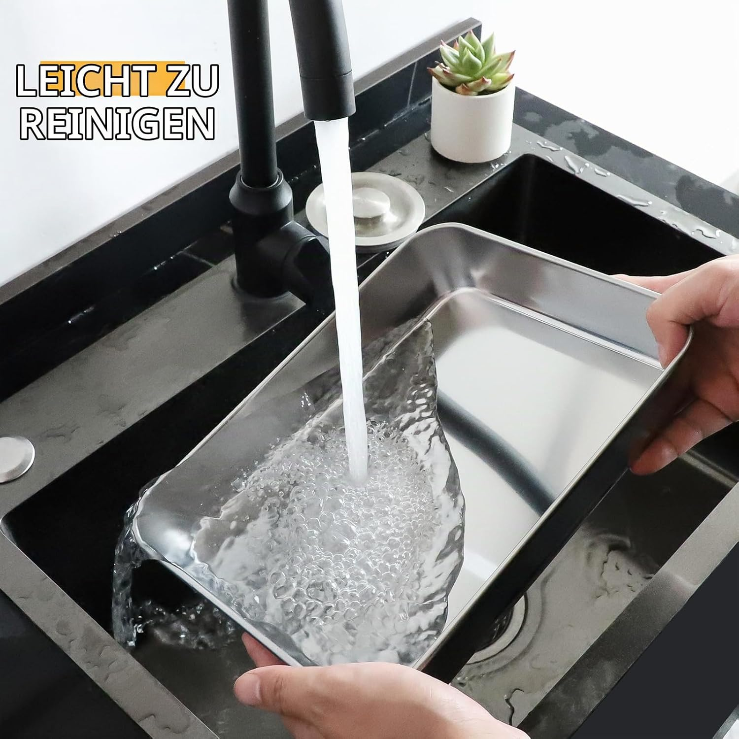 Eine Person wäscht ein Edelstahlblech unter fließendem Wasser in einer schwarzen Spüle.