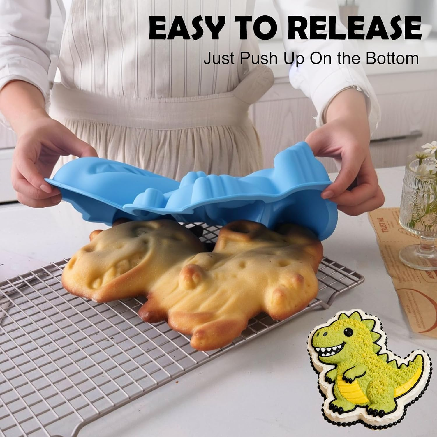 Eine Person hebt eine blaue Silikonform von zwei gebackenen Dinosauerkuchen auf einem Kuchengitter ab.