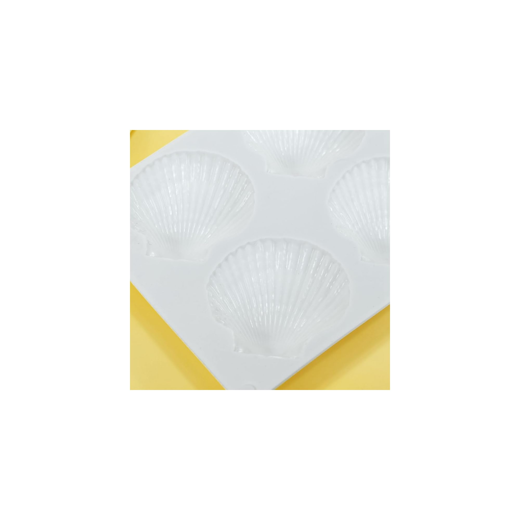 Eine weiße Silikonform mit Muschelmustern liegt auf einer gelben Oberfläche.