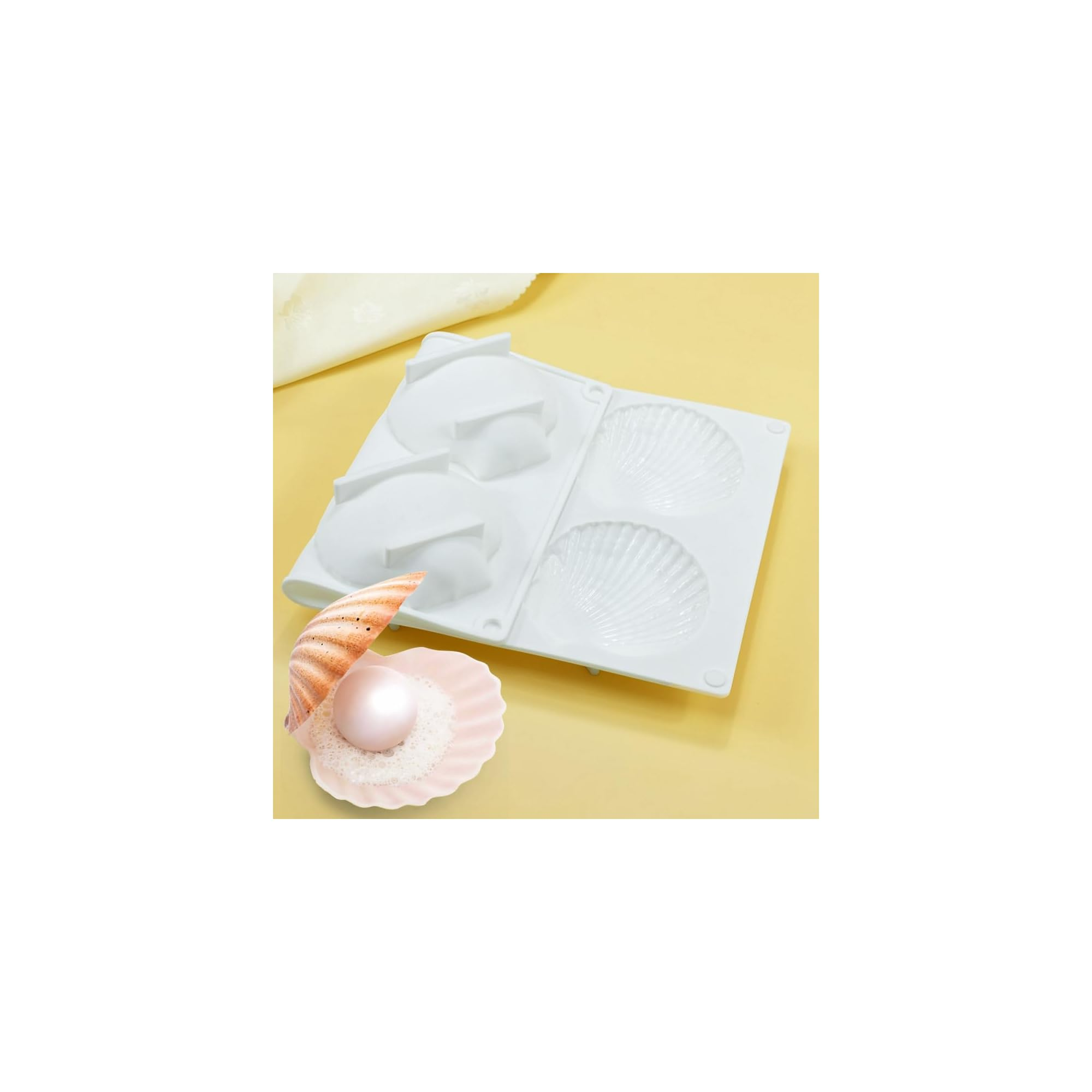Eine weiße Silikonform mit Muschelmuster und eine rosafarbene Muschel mit Perle auf gelbem Grund.