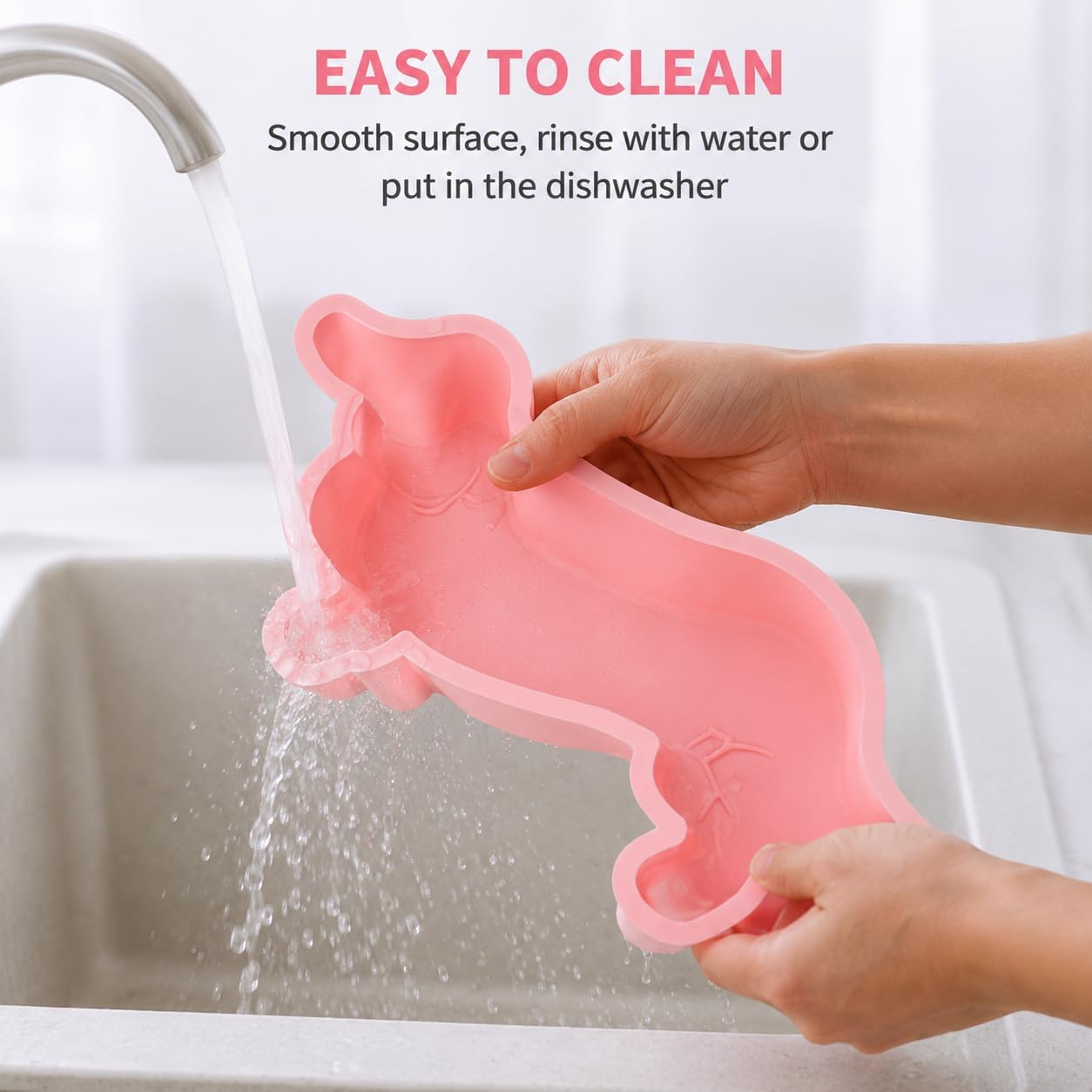 Eine Person spült eine rosa dackelartige Silikonform unter einem Wasserhahn ab.
