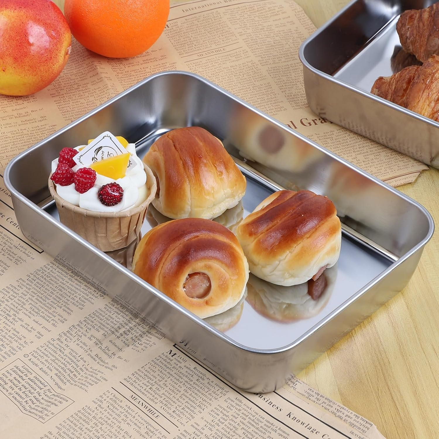 Frische Brötchen und ein Cupcake mit Beeren in Edelstahlbehälttern auf Zeitungspapier.