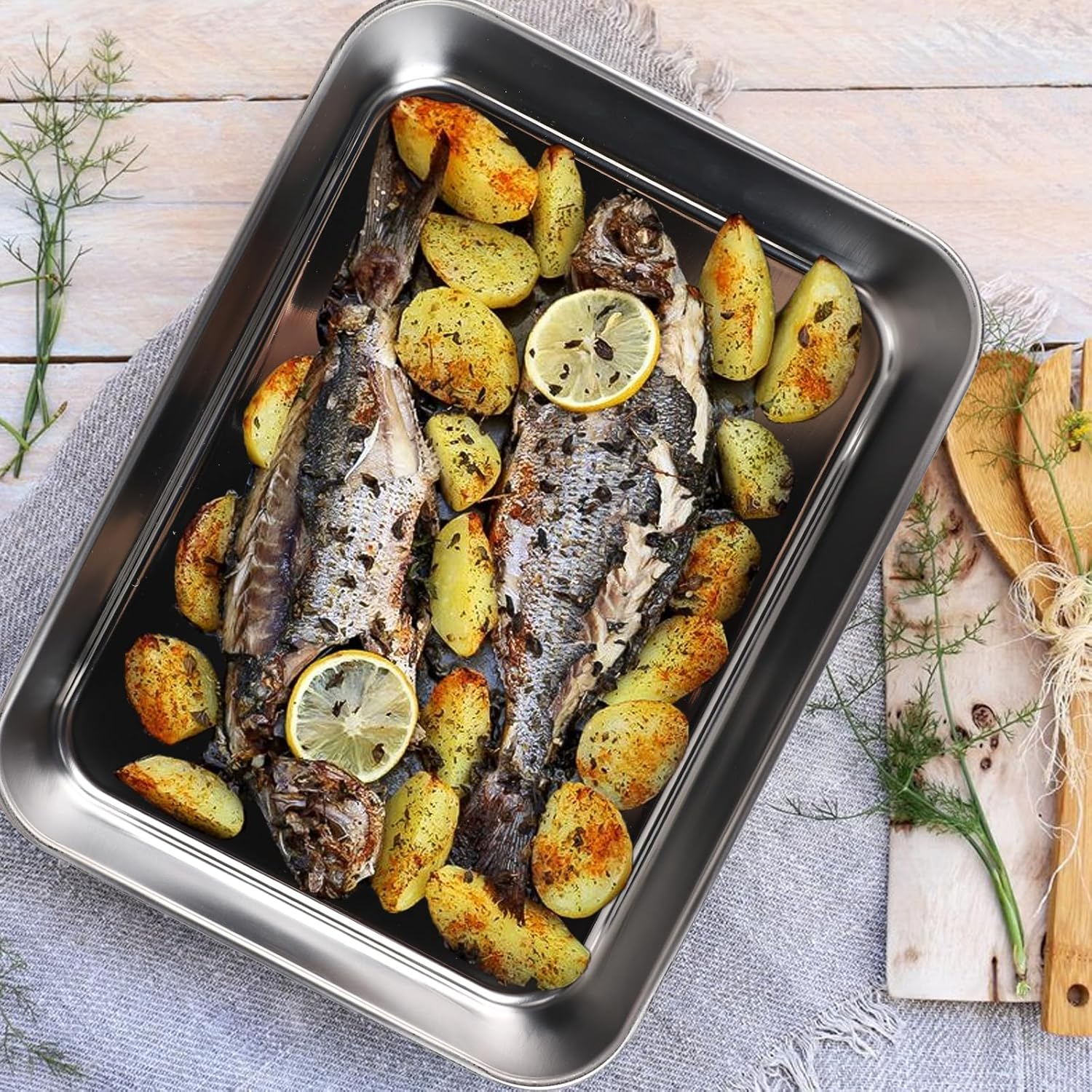 Gebratener Fisch und Kartoffeln in einer Silberform mit Zitronenscheiben.