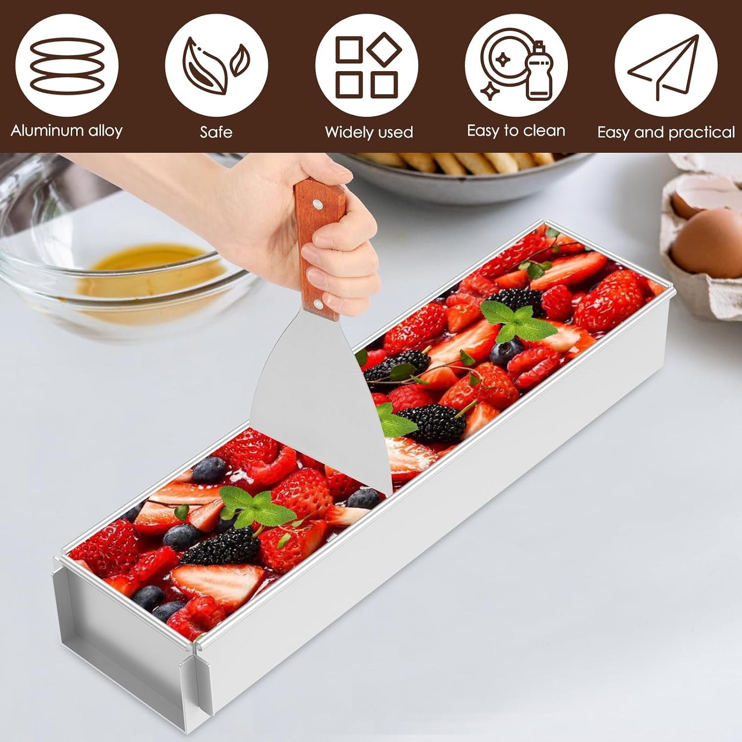 Eine Hand schneidet Kuchen mit Beeren in einer langen Alubackform auf einem Küchentisch.