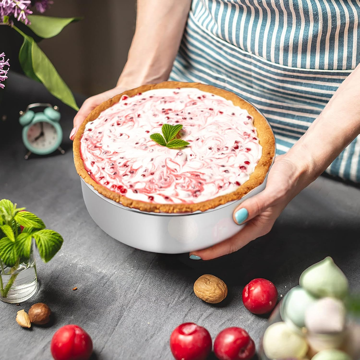 Eine Person im blau-weißen Apron hält eine große Beerentorte mit Minzblättern auf dem Tisch.