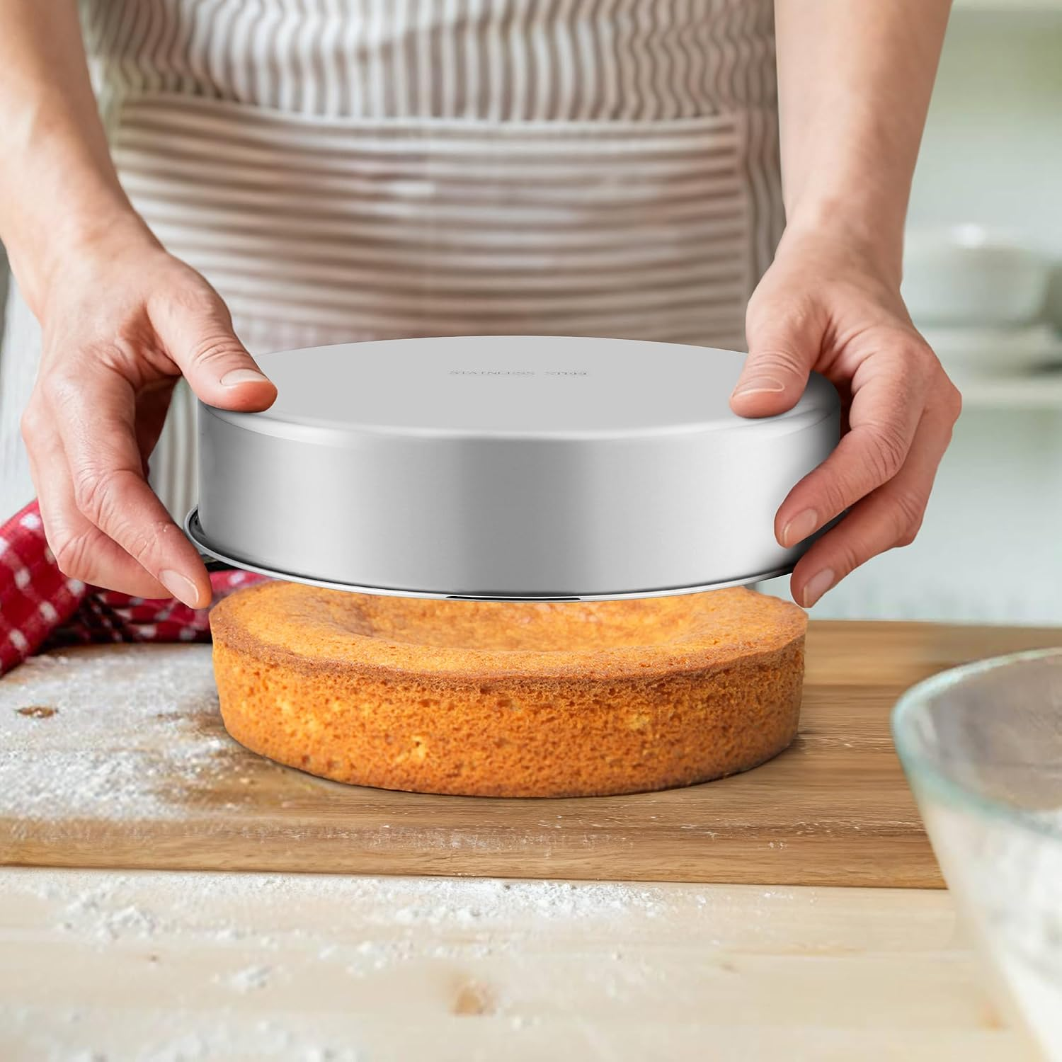 Eine Person hebt eine Edelstahl-Kuchenform von einem gebackenen runden Kuchen auf einem Holzbrett.