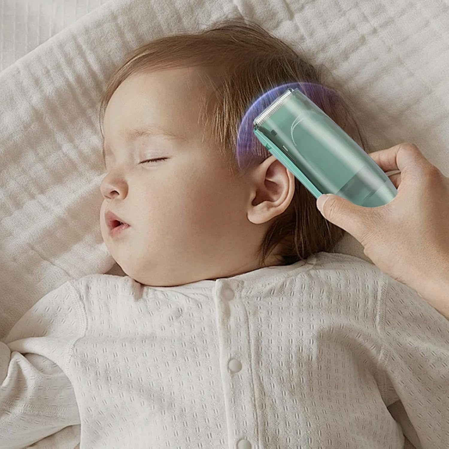 Eine Hand hält einen hellblauen Haarschneider nahe an den Kopf eines schlafenden Babys auf einer weißen Decke.